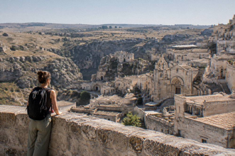A traveller with a backpack looking out over the Sassi rooftops toward the Murgia plateau