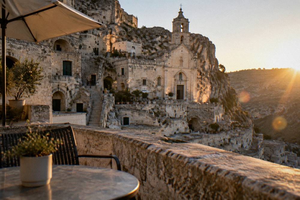 Rock-cut church facade and cave facades lit at dusk seen from a hotel terrace in Matera