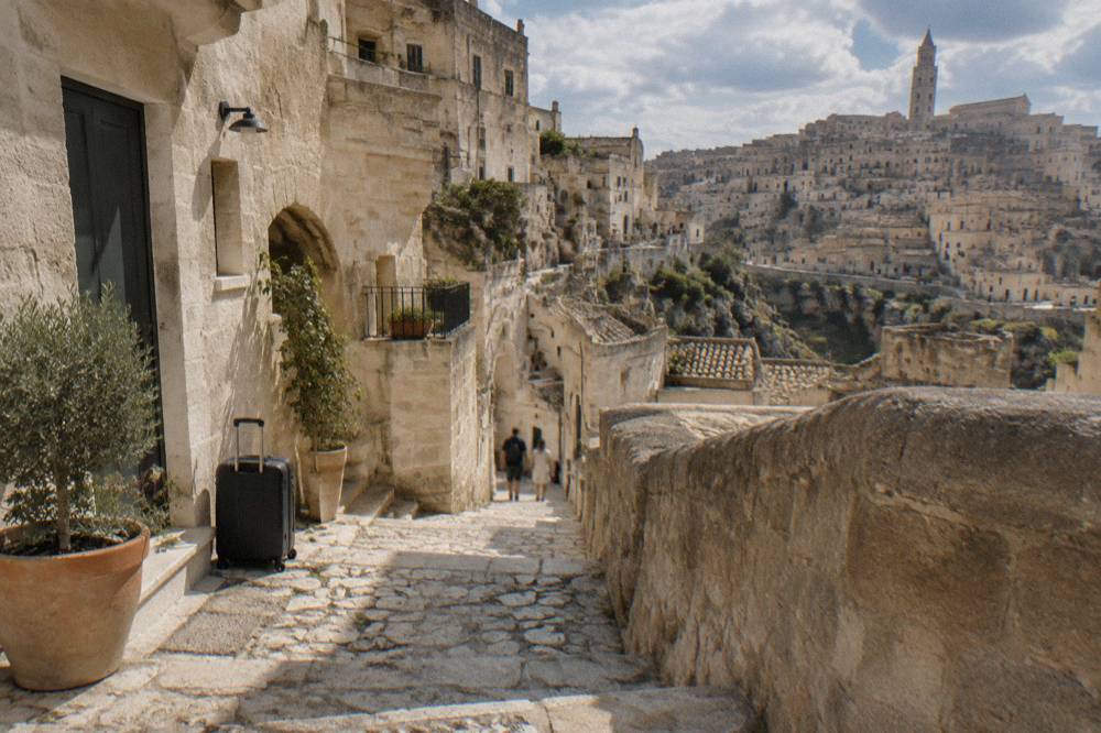Narrow stone stairway lane between cave hotel facades in Matera with luggage set down beside it