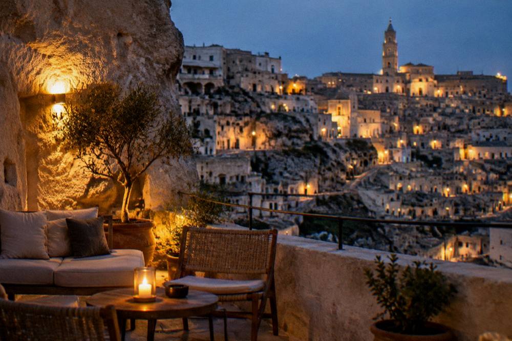 Warmly lit cave hotel terrace at night with the illuminated Sassi of Matera beyond