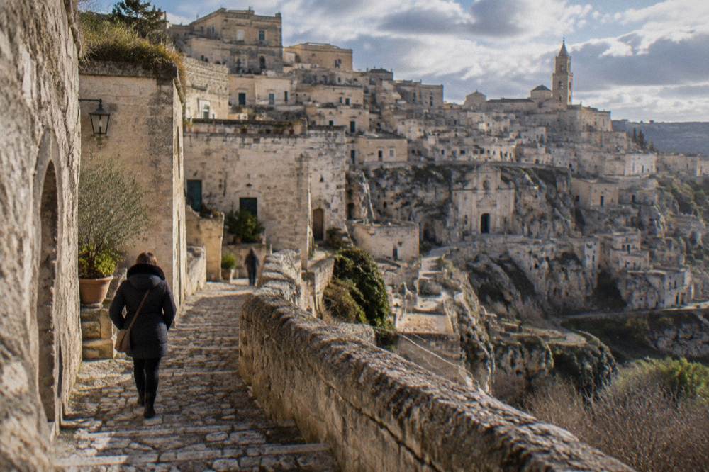 A visitor in a warm coat walking a narrow stepped lane in the Sassi in December