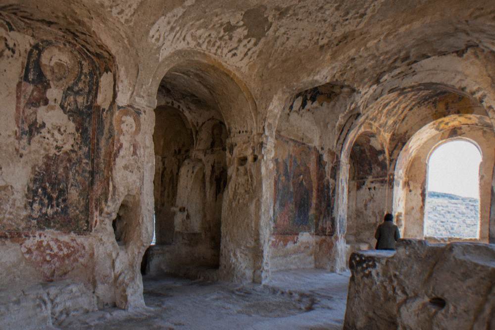 Interior of a rock-cut church with carved arches and fresco fragments in Matera