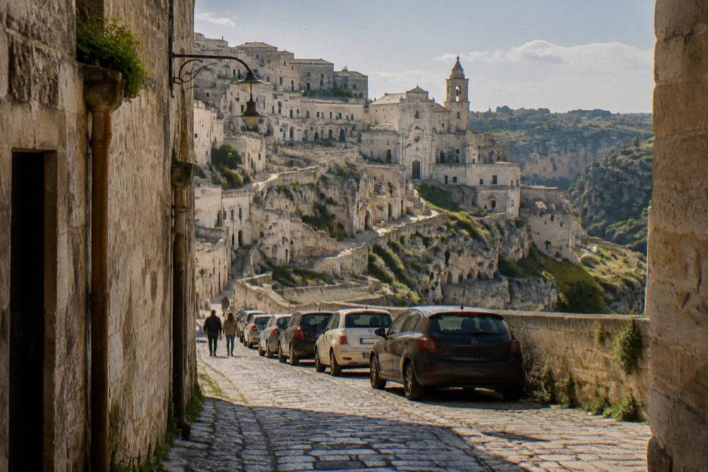A narrow stone street in Matera lined with parked cars near the edge of the ZTL