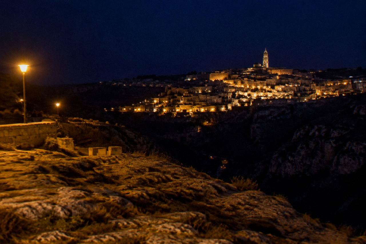 The illuminated cave dwellings of the Sassi districts glowing above the dark Gravina canyon at night
