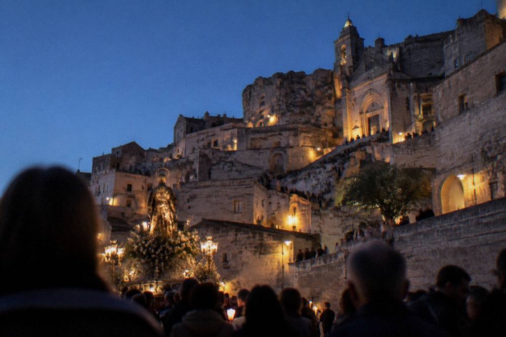 A crowd watching a floodlit procession move through a stone square at night