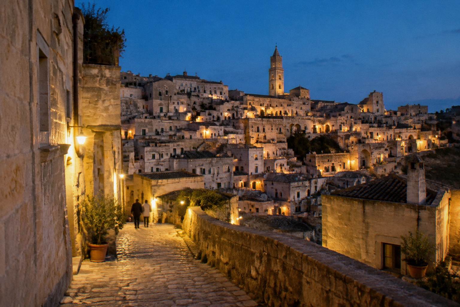 Stone houses of the Sassi lit by warm street lamps against a deep blue sky