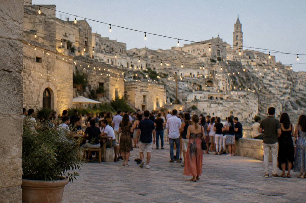 Crowds holding a summer evening celebration in a Matera square with lights strung overhead