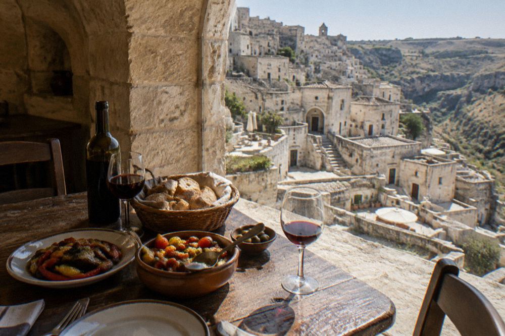 A rustic table with bread, wine and vegetable dishes in a stone-vaulted dining room