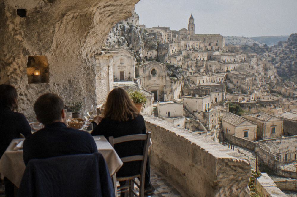Diners seated at a table set against rough tufa stone walls in a cave restaurant