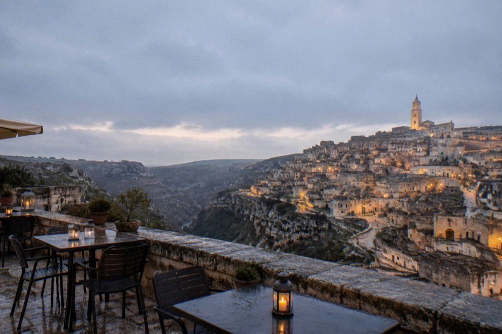 Terrace tables overlooking the illuminated Sassi and the dark canyon at dusk