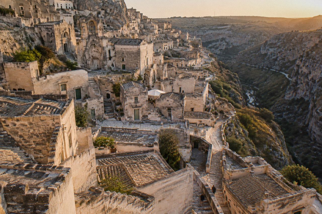 Cave dwellings and stone houses stacked along the side of the Matera gorge at dusk