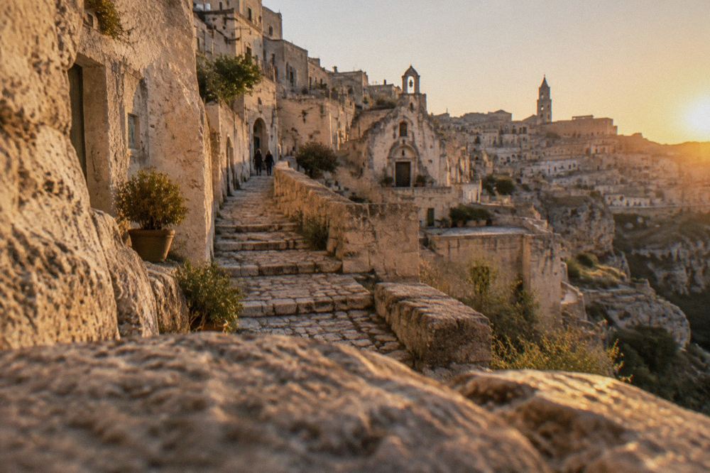 A narrow stepped lane climbing between pale stone cave facades in the Sassi