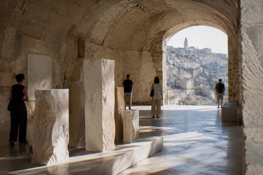Visitors viewing contemporary art installations inside a stone-vaulted museum hall in Matera