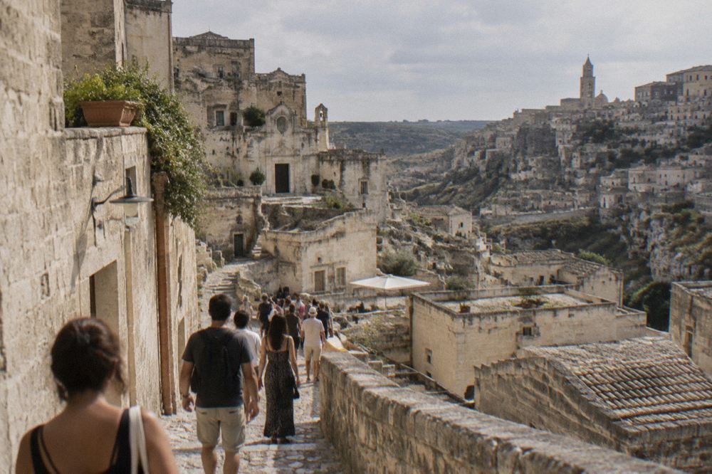 Crowd of visitors walking through a narrow stepped lane in the Sassi on a warm evening
