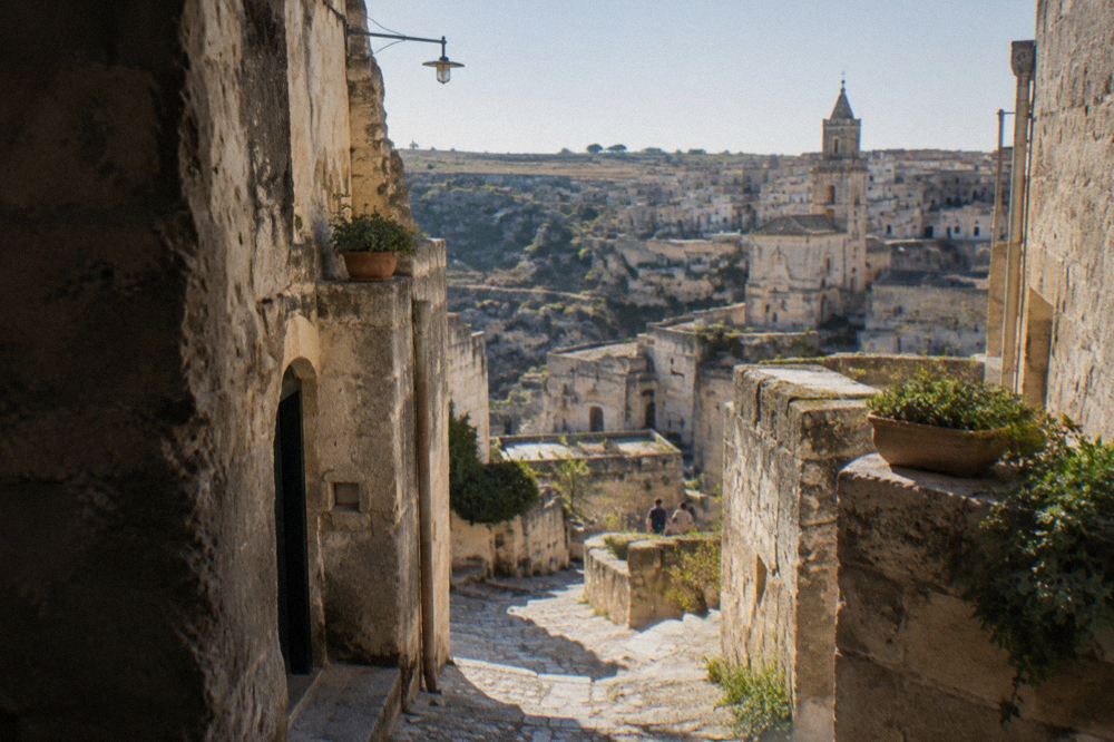 A narrow stepped lane between stone cave houses in the Sassi under strong midday light