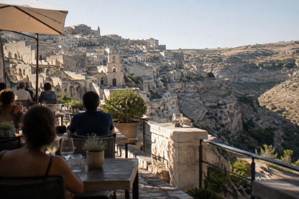 An evening crowd at an outdoor restaurant terrace above the cave houses of Sasso Caveoso