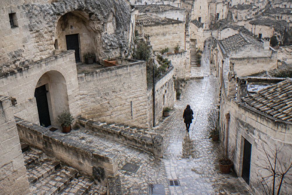 An empty stone street in Sasso Barisano in winter, with cave doorways and a single figure in a coat