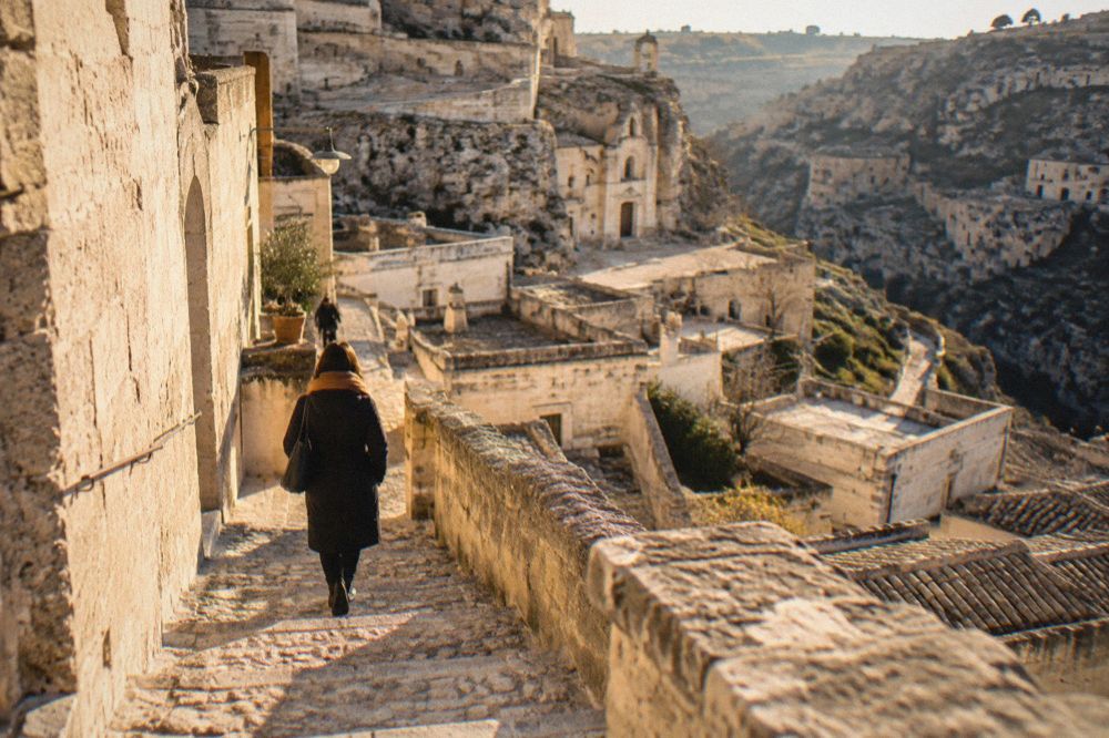 A traveller in a warm coat and scarf walking a stone stairway between cave houses in Matera in winter