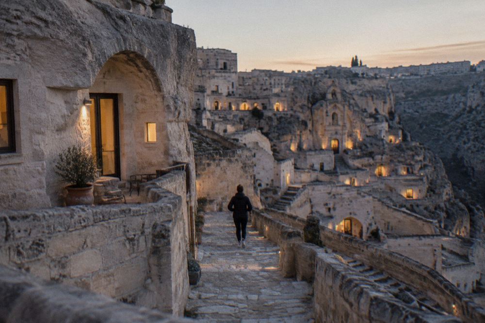 The warm lit windows of cave hotel rooms set into a stone facade in the Sassi at dusk in winter