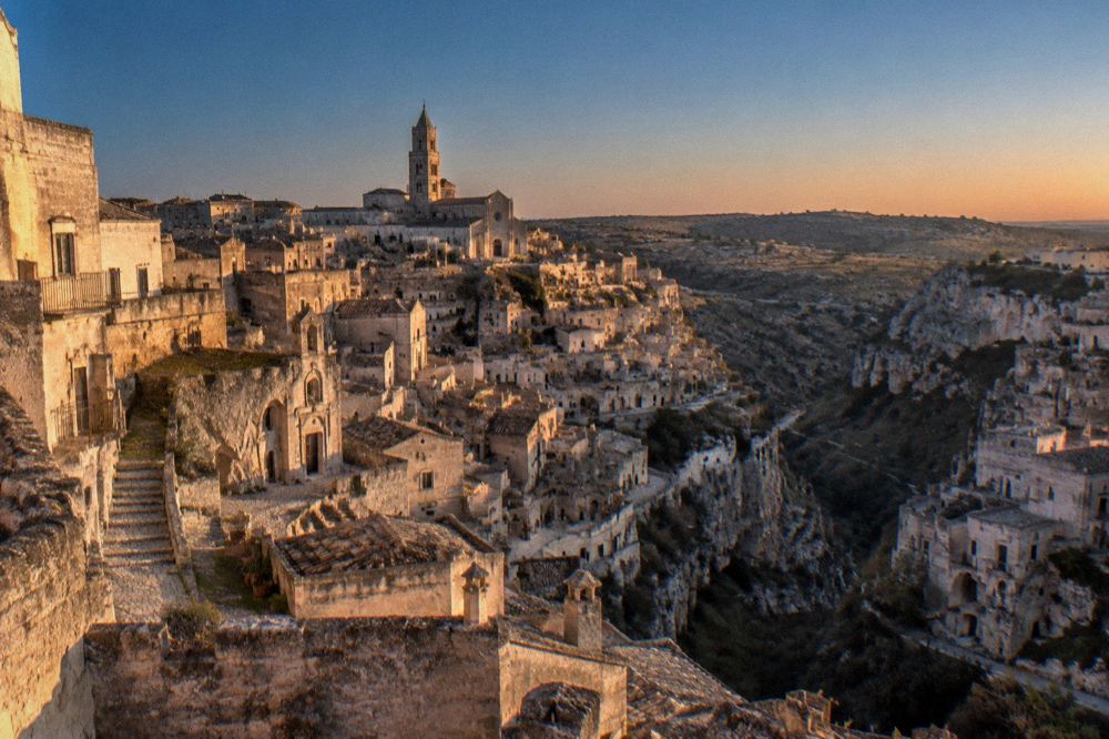 Matera's Sassi and the Cathedral silhouette seen at dusk under a deep blue winter sky, with the Murgia plateau beyond