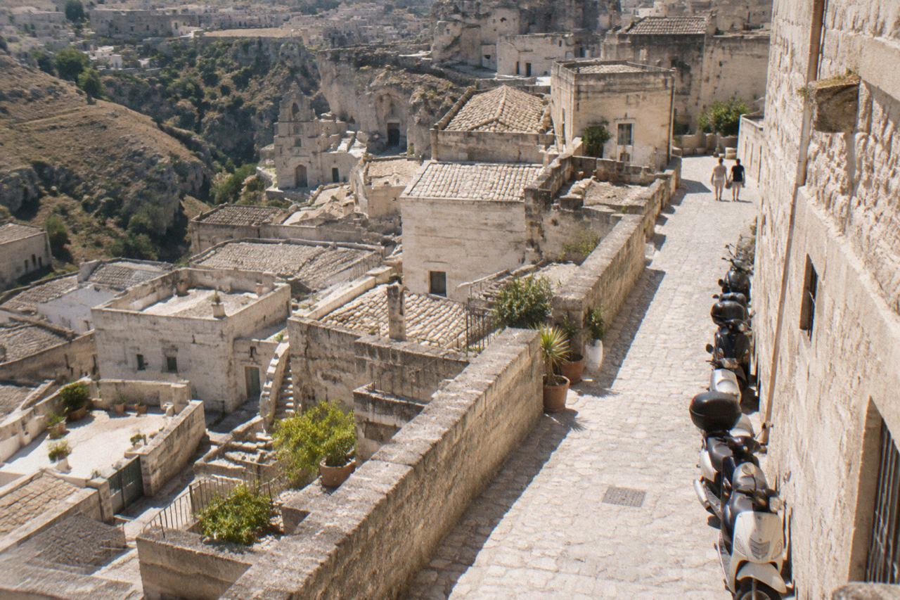 A narrow stone street in the Sassi of Matera with parked scooters along a pale tufa wall
