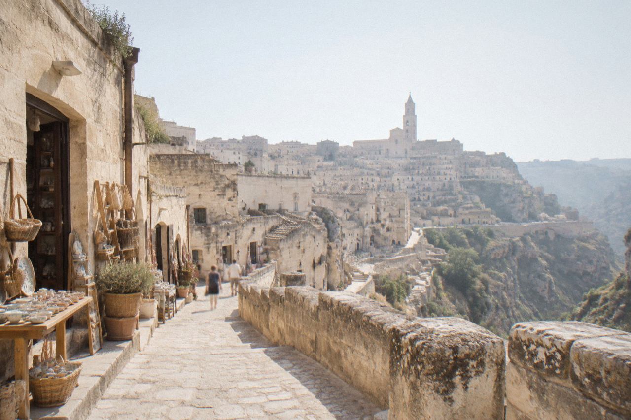 A stone lane in the Sassi of Matera with small shop doorways and artisan goods displayed outside