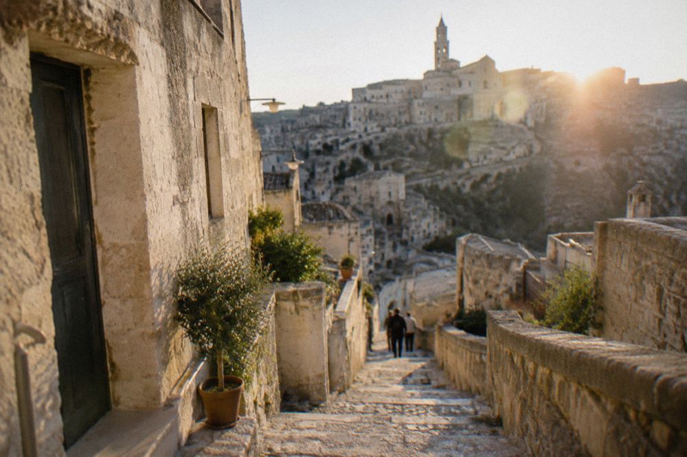 A narrow stepped street in Matera with shop signs and stone walls in warm afternoon light