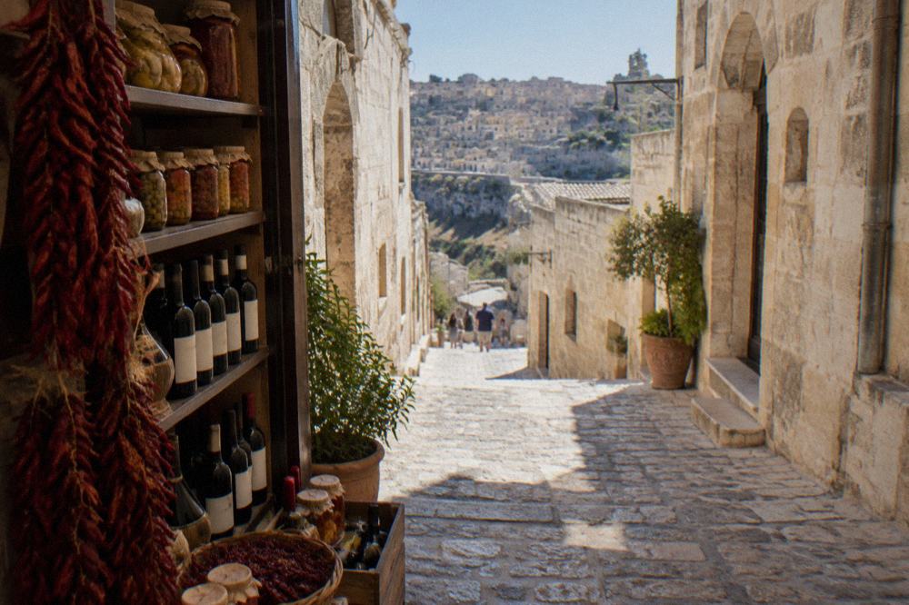 Bags of dried red peppers, jars of preserves and bottles of wine on the shelves of a small Italian food shop