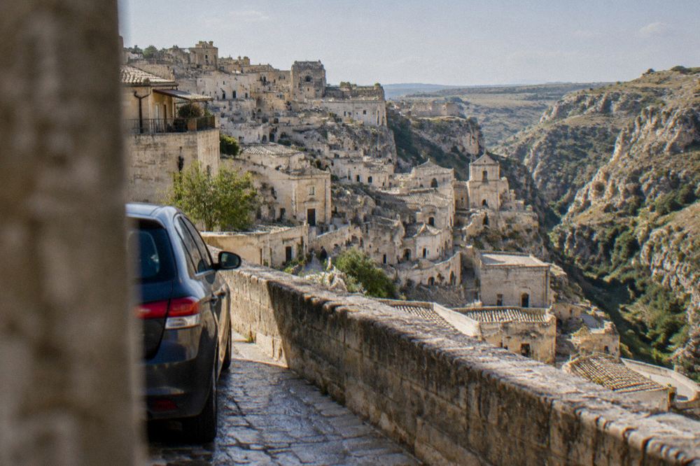 A parked car on a street above the Sassi with the cave city and canyon visible below