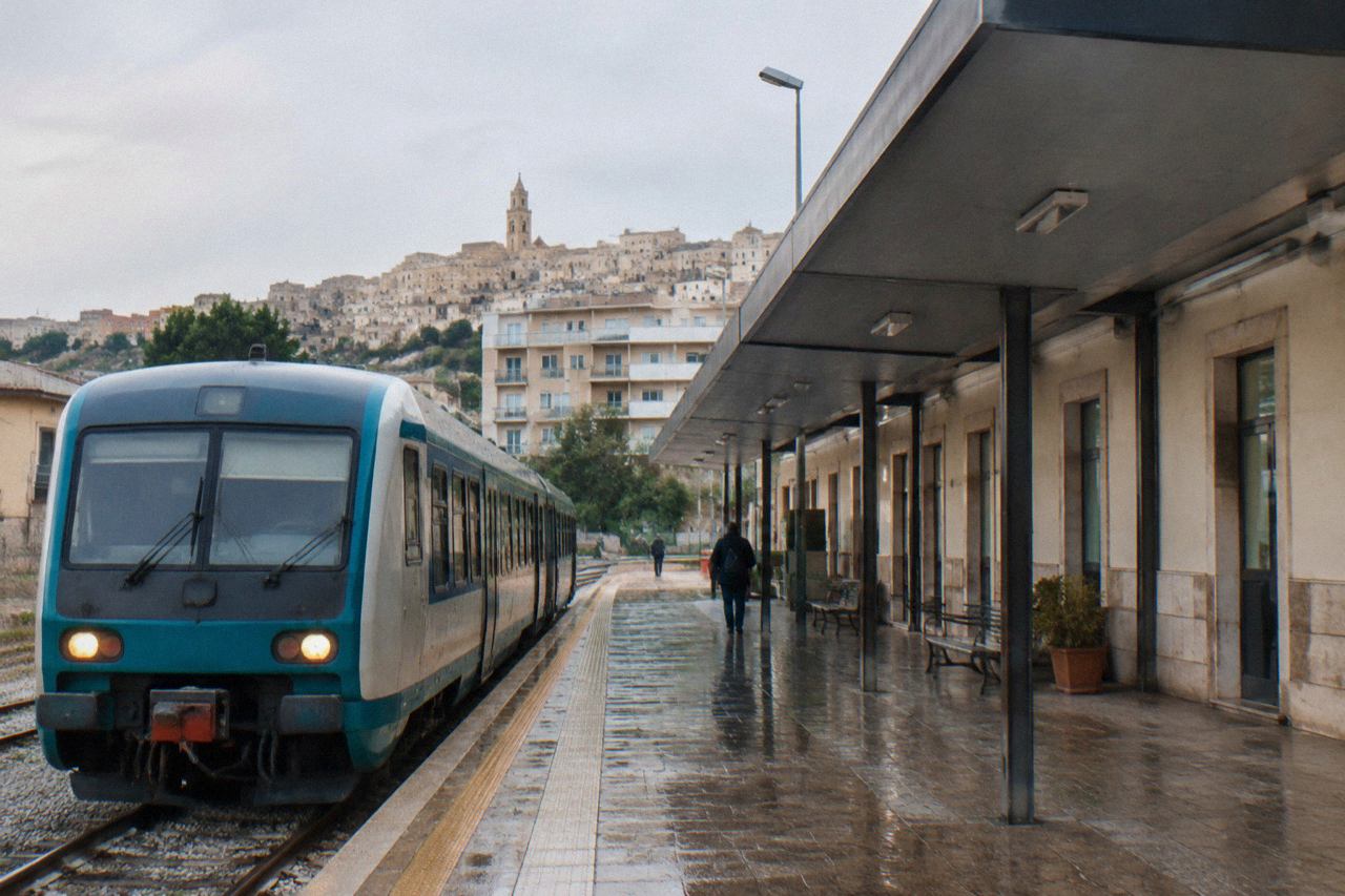 A small regional train standing at a platform beside a modern station building in southern Italy