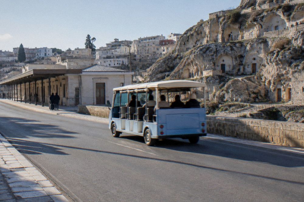 An open-top small electric sightseeing bus driving past cave houses on a panoramic road