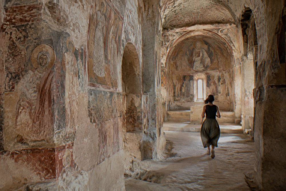 Interior of a rock-cut church in Matera with frescoed walls lit softly