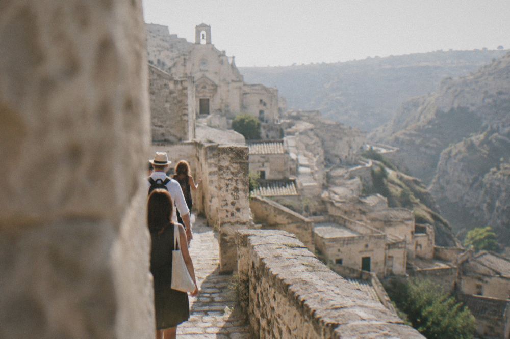 A small group of visitors following a guide along a narrow stone lane in Matera
