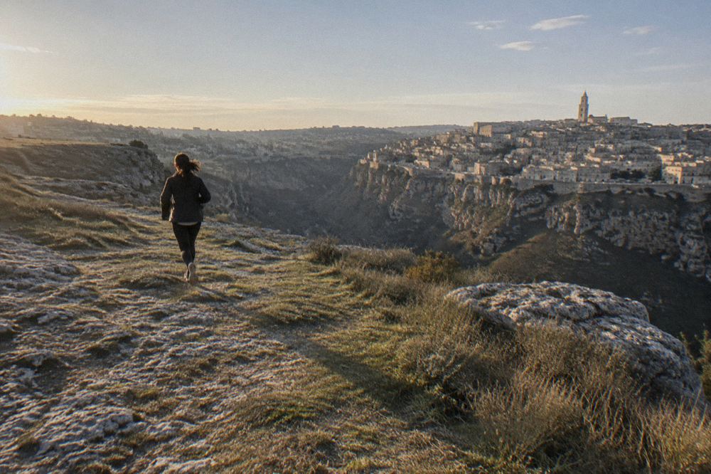 Wide view across the Gravina canyon to the clustered stone facades of Matera at dawn