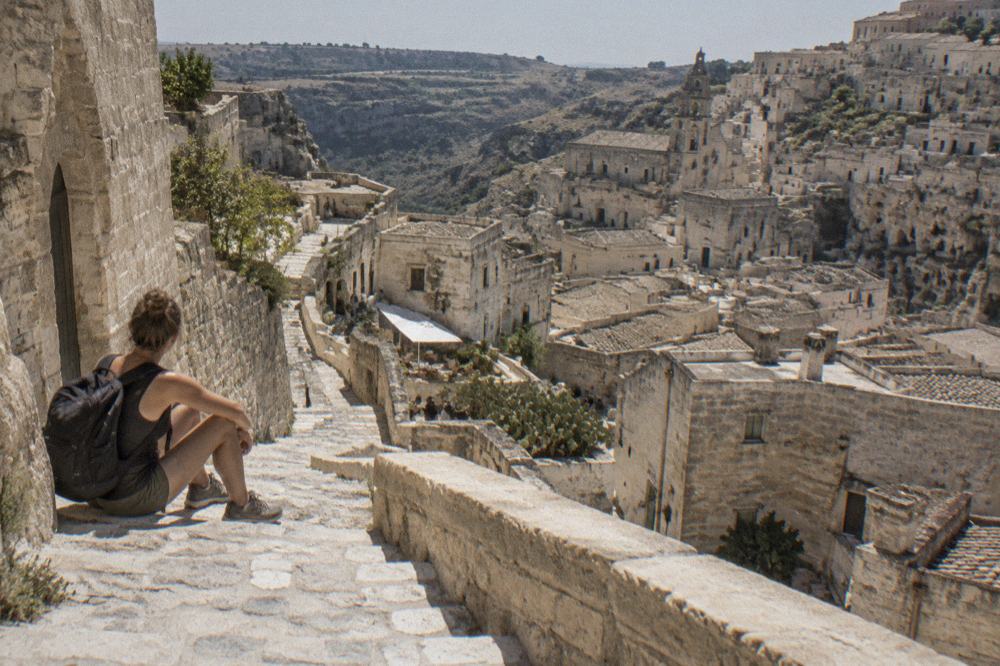 A visitor in walking shoes resting on a stone stair in a Sassi lane