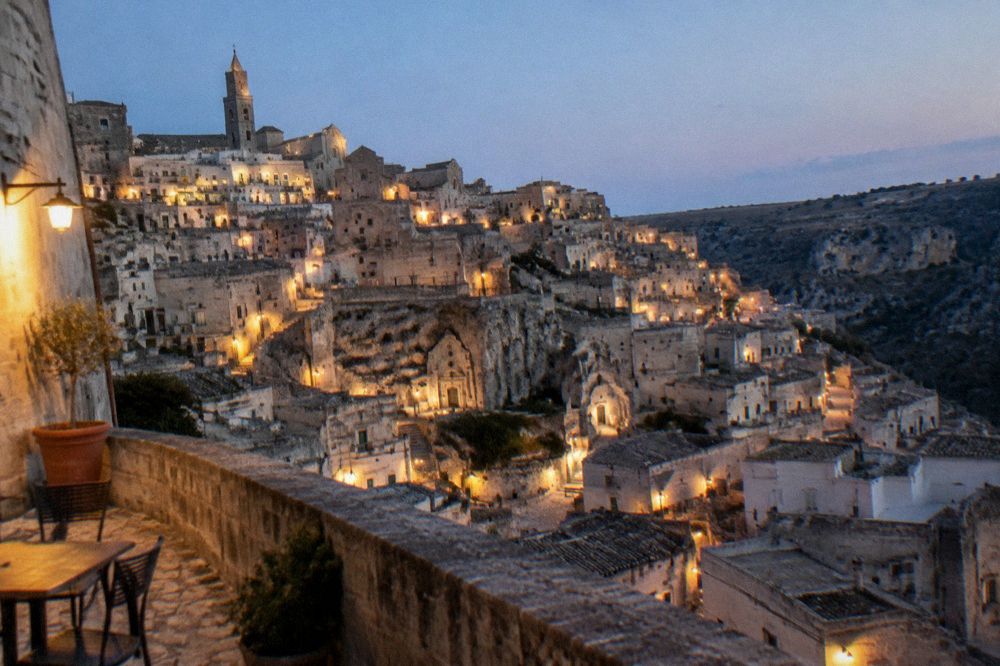 An evening view over the illuminated Sassi rooftops from a stone terrace