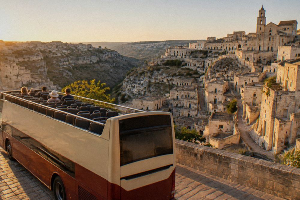 An open-top panoramic sightseeing bus parked on a street above the Sassi districts