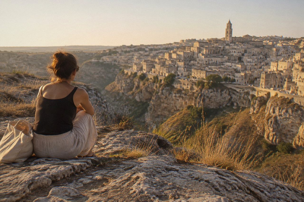 The Sassi cave district of Matera under a clear sky, with pale stone buildings stacked along the edge of the Gravina canyon