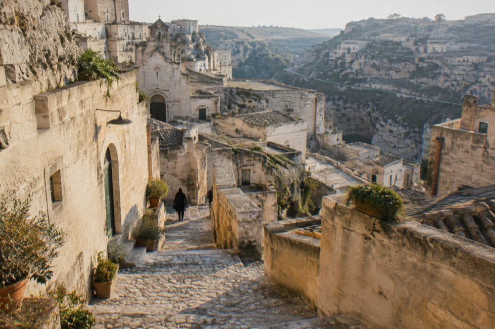 A stone stairway between pale cave buildings in the Sassi of Matera in warm morning light