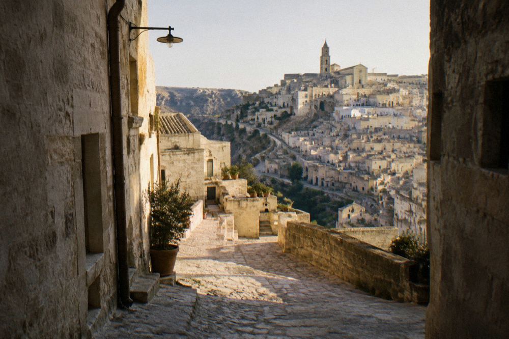 A shaded lane in Matera with pale stone walls glowing in strong afternoon sun