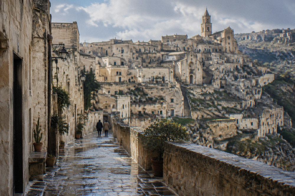 Wet stone paving in a narrow Matera street reflecting the pale facades after rain