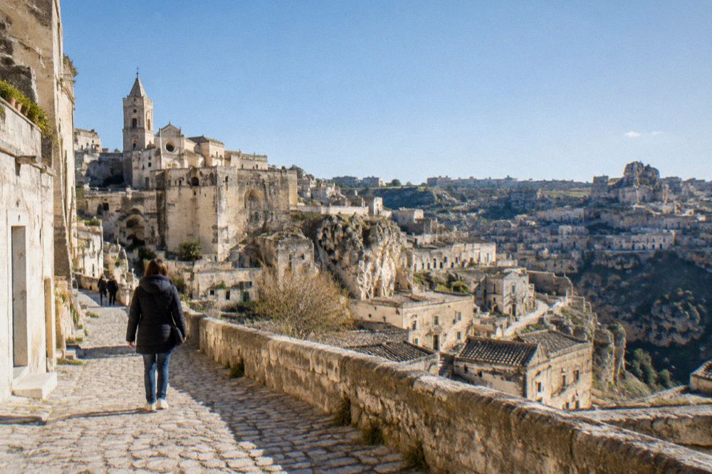 A visitor in a warm jacket walking a cobbled lane in Matera on a cool clear day