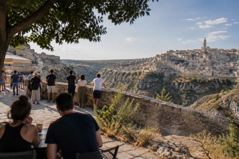 A busy panoramic terrace in Matera overlooking the Sassi and the Gravina canyon in late afternoon light