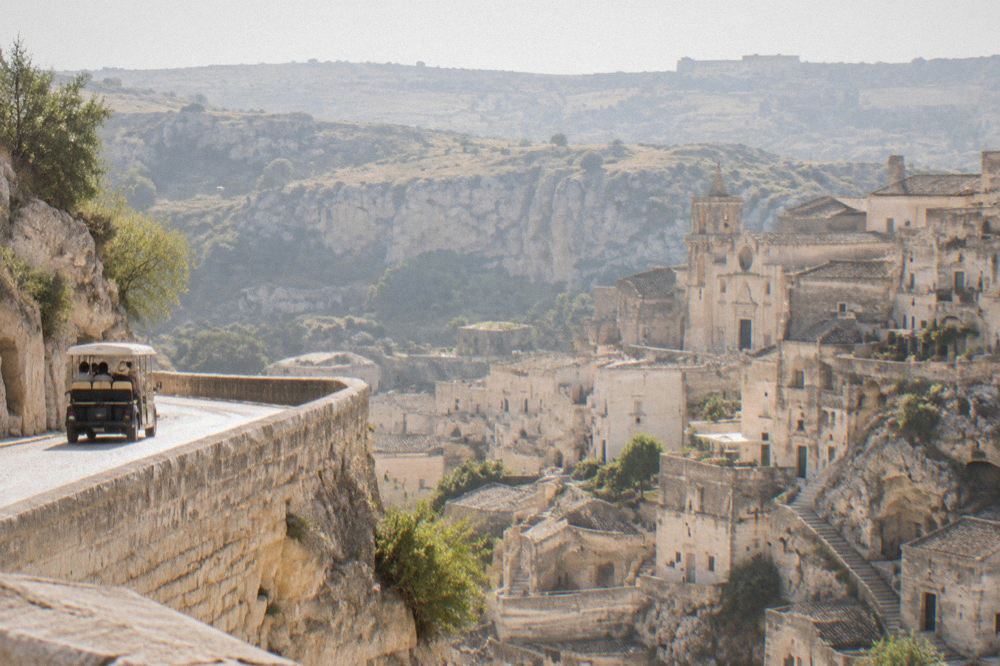 A small open tour vehicle on a panoramic road above Matera with the Sassi below