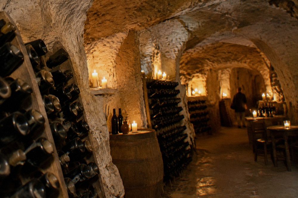 A candlelit cave cellar in Matera with bottles racked against rough tufa stone walls