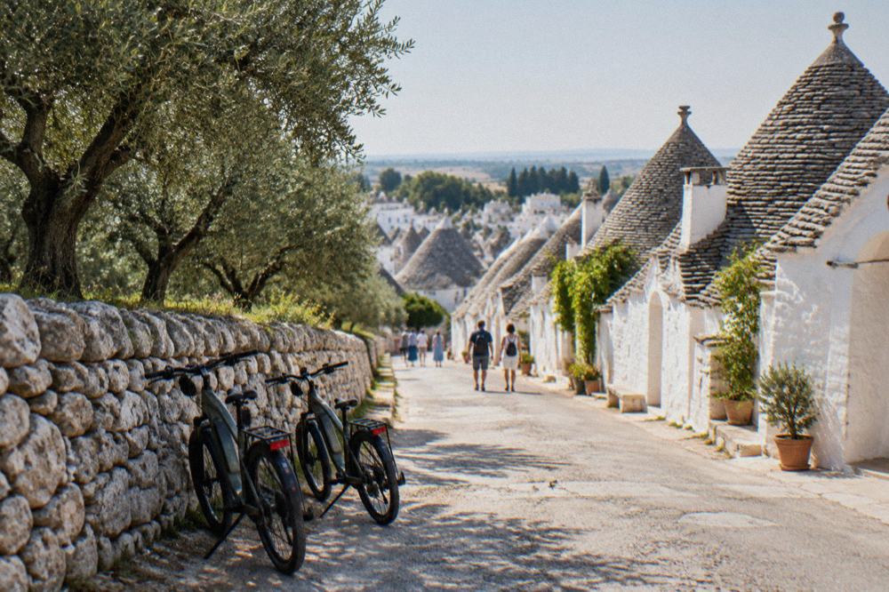 Electric bicycles parked on a country lane between dry-stone walls and olive trees near Alberobello