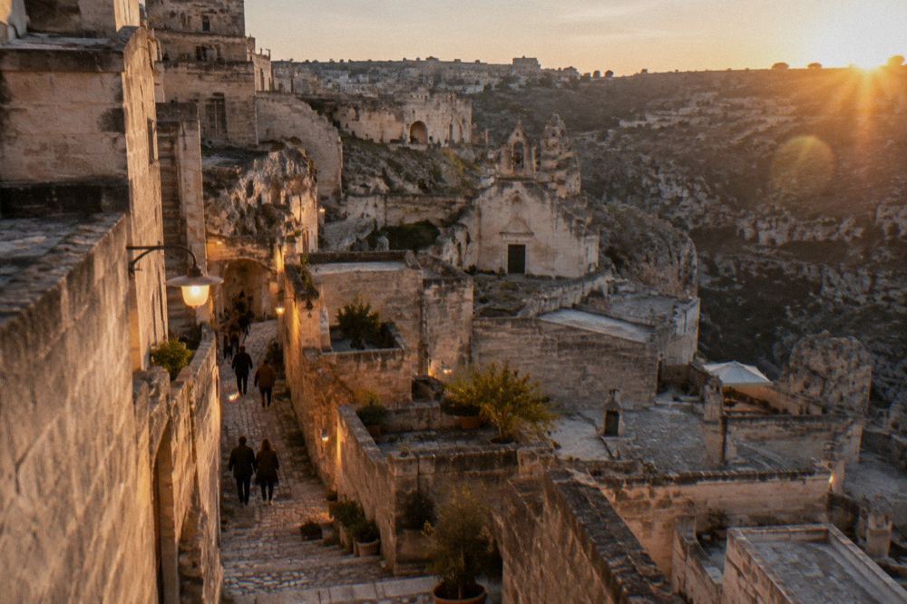 An evening street in the Matera Sassi lit by warm lamps with people walking between stone buildings
