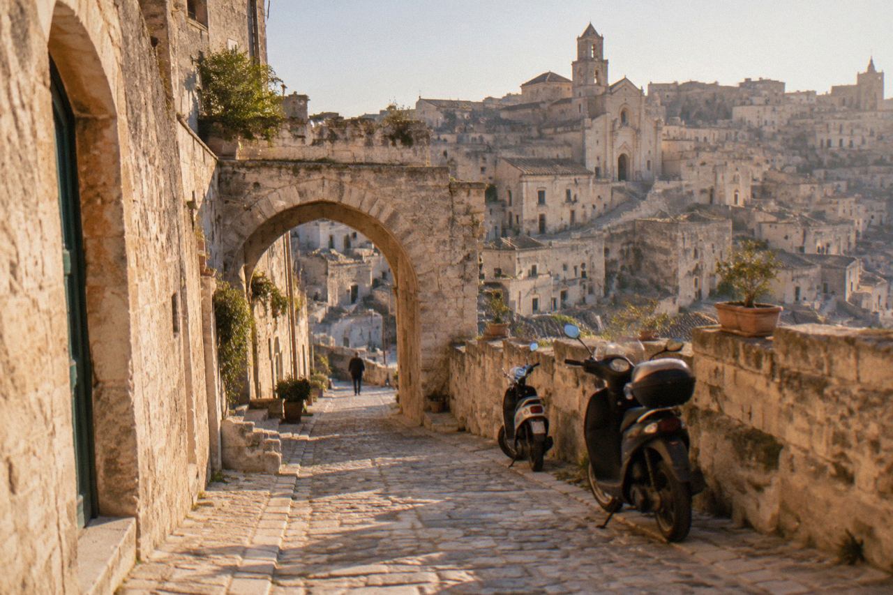 A narrow stone street in the Sassi of Matera with an arched gateway and parked scooters