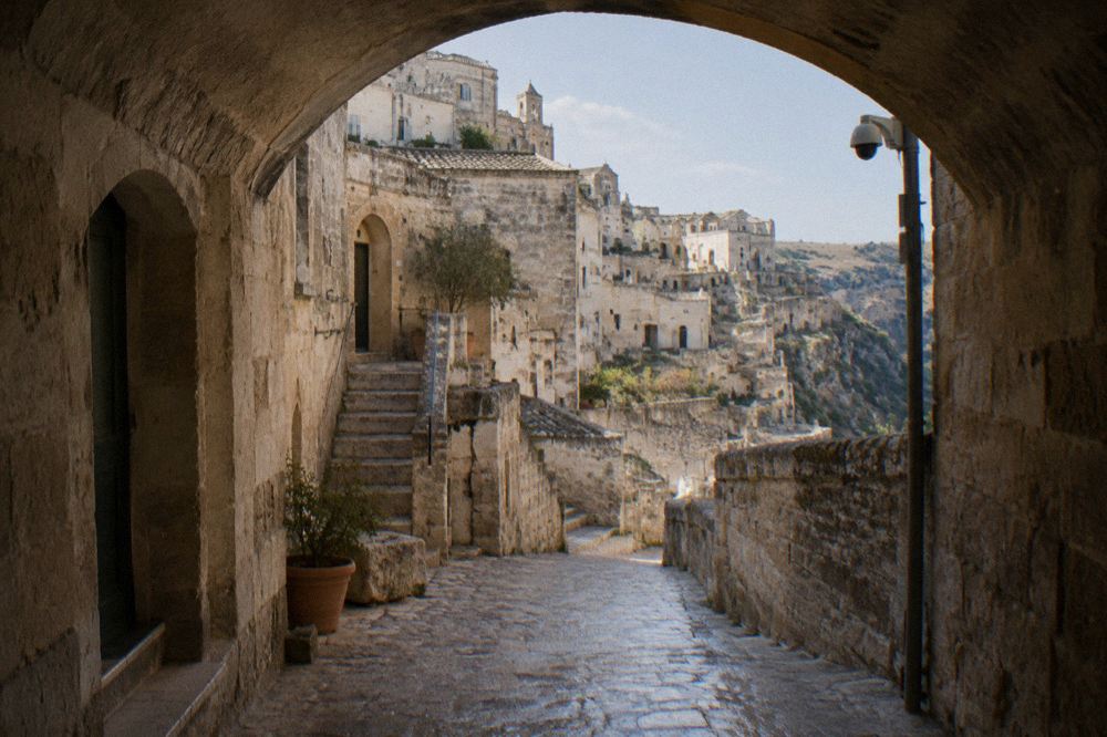 A stone archway over a lane in Sasso Barisano with a camera-mounted pole visible nearby