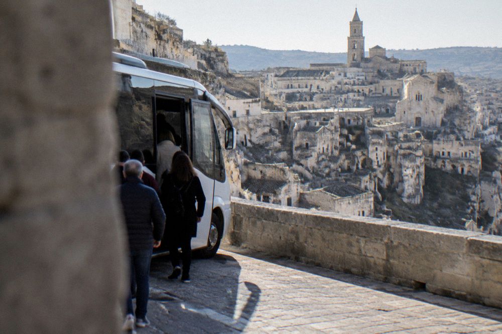 A tour minibus parked on a street above the Sassi of Matera with passengers boarding